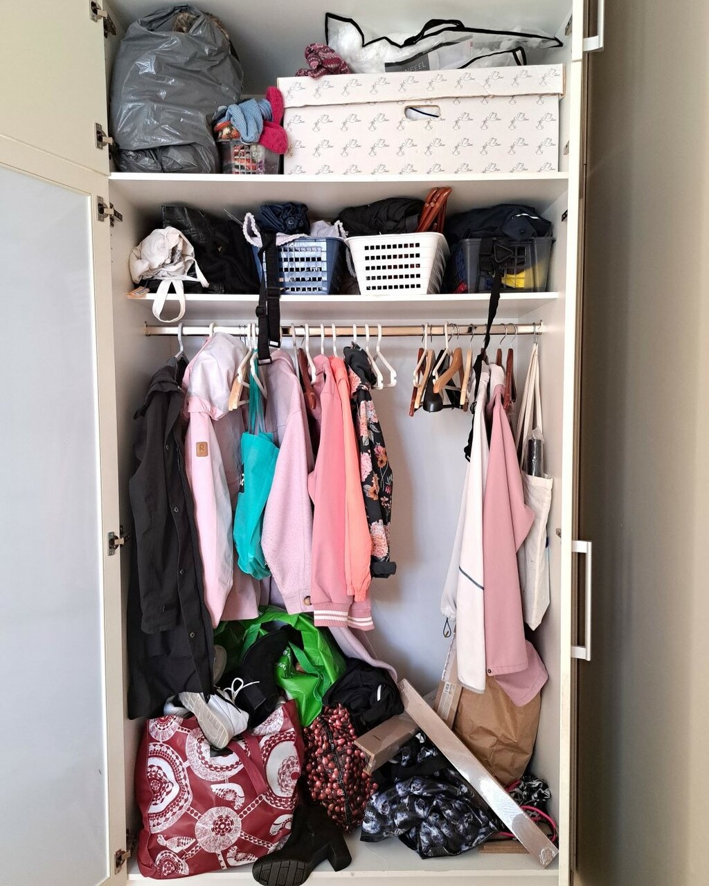 Vaatekaapissa on ulkovaatteiden lisäksi monenlaista muuta tavaraa. Säilytyskorit ja kassit pursuavat tavaraa.
